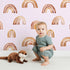 Lovely child standing in front of Whimsy Tots Boho Brush Rainbow Wallpaper in Pink with rainbow, stripe, arch in design. Lovely child standing in front of Whimsy Tots Boho Brush Rainbow Wallpaper in Pink with rainbow, stripe, arch in design.