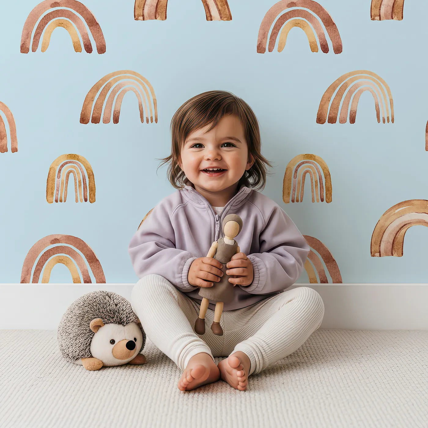 Lovely child standing in front of Whimsy Tots Boho Brush Rainbow Wallpaper in Blue with rainbow, stripe, arch in design.