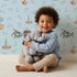 Lovely child standing in front of Whimsy Tots Seaside Vessel Parade Wallpaper in Blue with boat, submarine, splash, sail in design. Lovely child standing in front of Whimsy Tots Seaside Vessel Parade Wallpaper in Blue with boat, submarine, splash, sail in design.