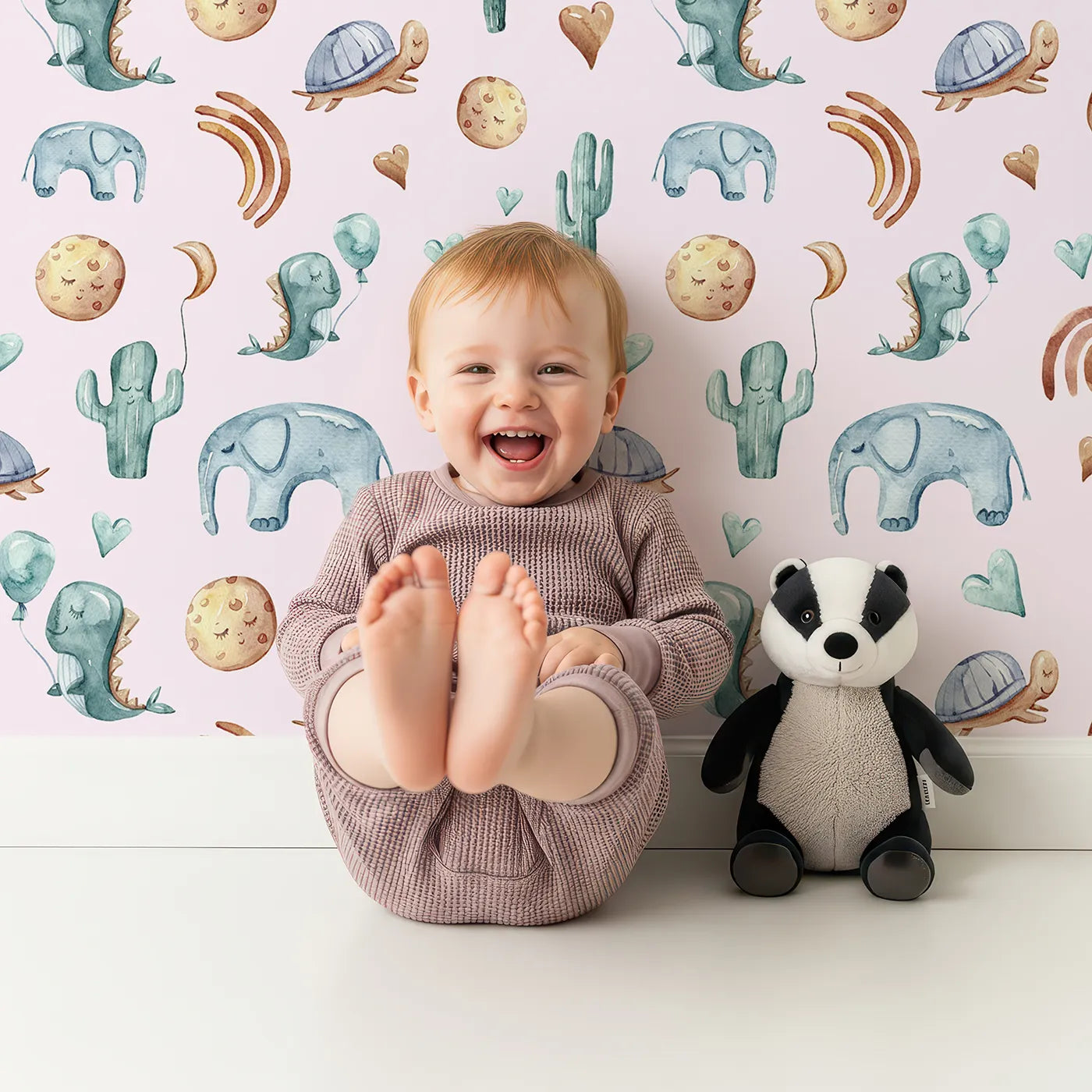 Lovely child standing in front of Whimsy Tots Balloon Friends Parade Wallpaper in Pink with dinosaur, elephant, turtle, cactus, moon, heart, rainbow in design.