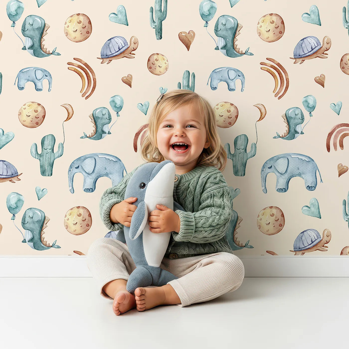 Lovely child standing in front of Whimsy Tots Balloon Friends Parade Wallpaper in Beige with dinosaur, elephant, turtle, cactus, moon, heart, rainbow in design.