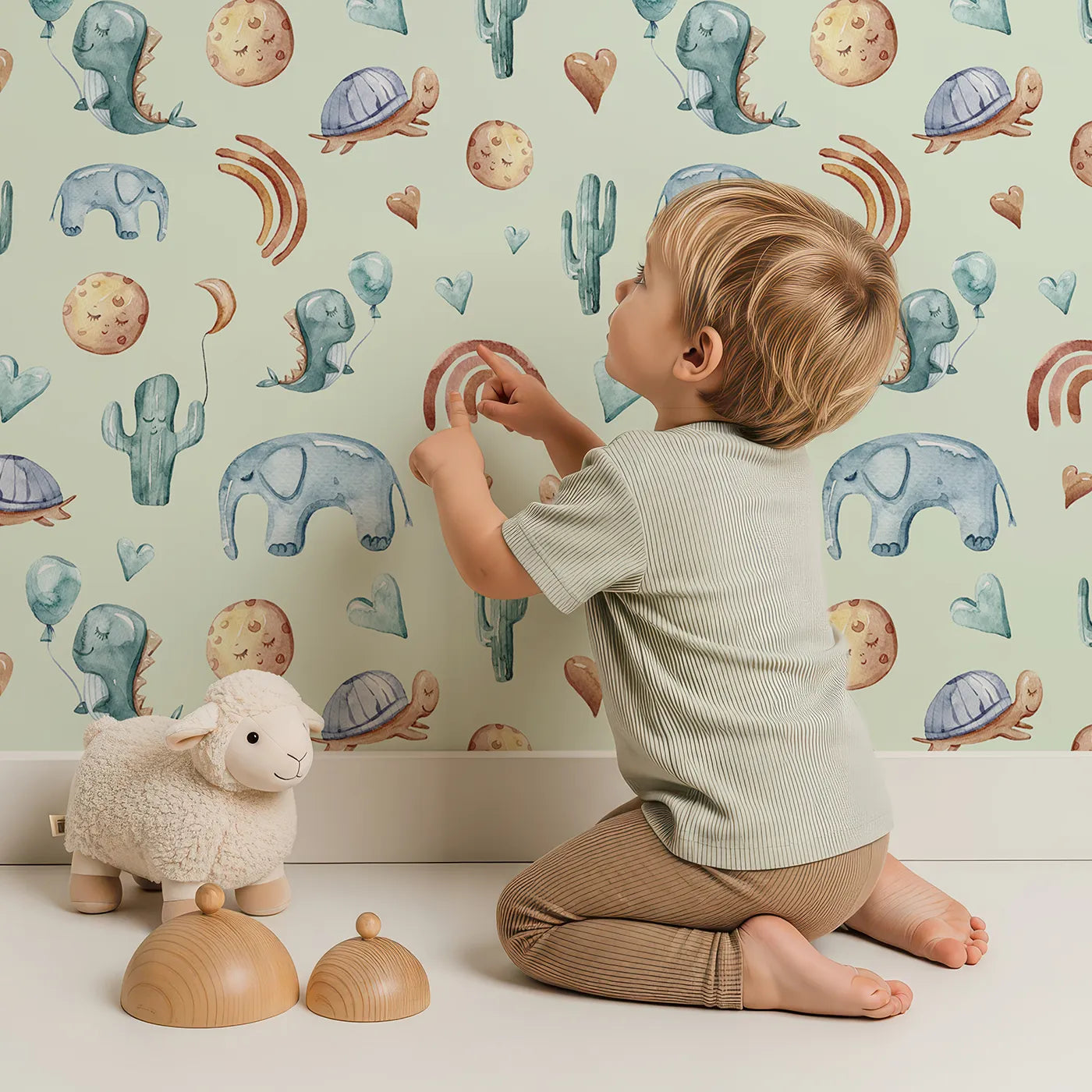 Lovely child standing in front of Whimsy Tots Balloon Friends Parade Wallpaper in Mint Green with dinosaur, elephant, turtle, cactus, moon, heart, rainbow in design.