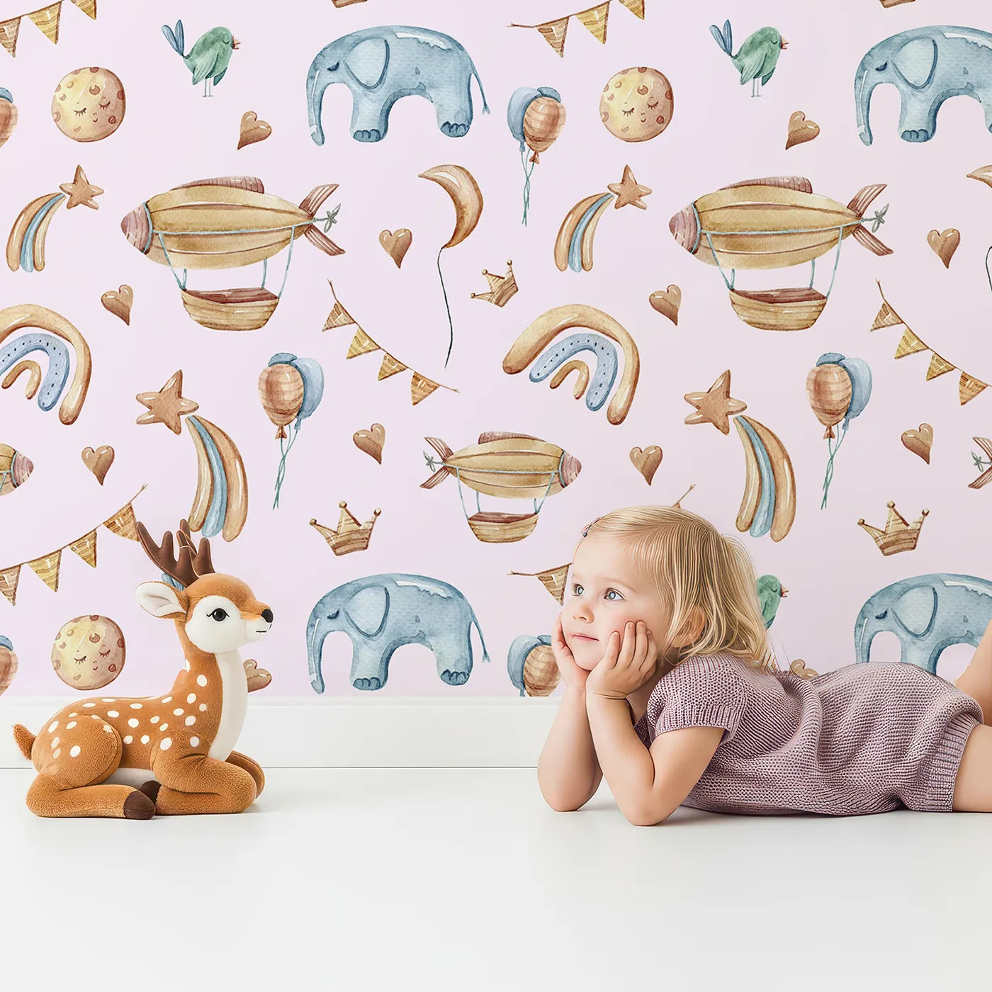 Lovely child standing in front of Whimsy Tots Sky Dreams Celebration Wallpaper in Pink with airship, balloon, crown, moon, rainbow, heart, elephant, bird in design.