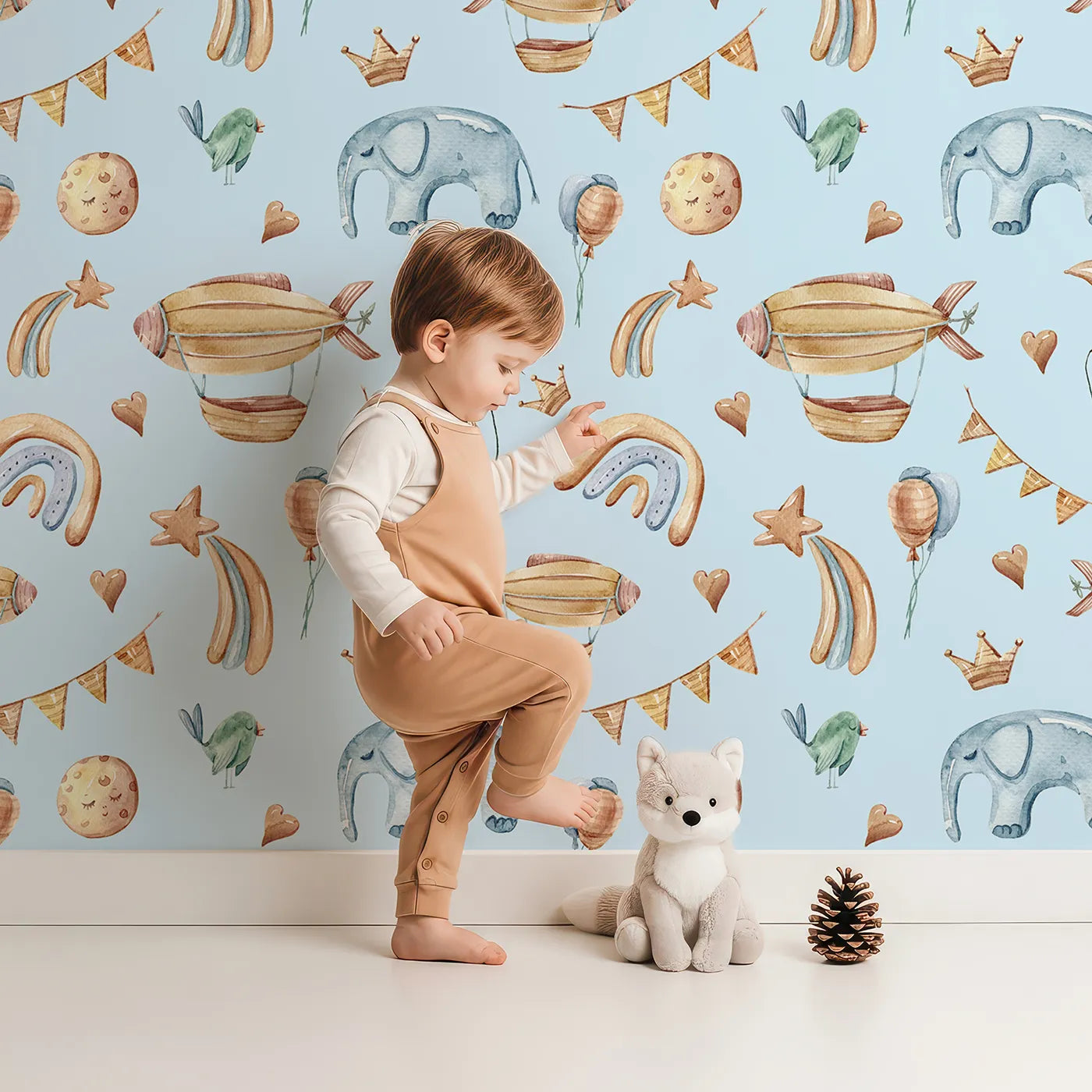 Lovely child standing in front of Whimsy Tots Sky Dreams Celebration Wallpaper in Blue with airship, balloon, crown, moon, rainbow, heart, elephant, bird in design.
