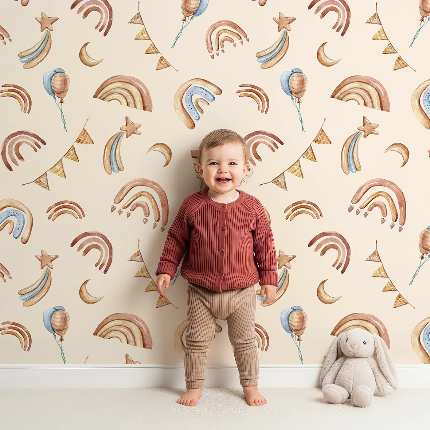 Lovely child standing in front of Whimsy Tots Sky Bloom Party Wallpaper in Beige with rainbow, balloon, moon, star, bunting, heart in design.