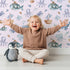 Lovely child standing in front of Whimsy Tots Deep Sea Discovery Wallpaper in Pink with whale, fish, submarine, jellyfish, seaweed, boat in design. Lovely child standing in front of Whimsy Tots Deep Sea Discovery Wallpaper in Pink with whale, fish, submarine, jellyfish, seaweed, boat in design.