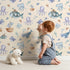 Lovely child standing in front of Whimsy Tots Deep Sea Discovery Wallpaper in Beige with whale, fish, submarine, jellyfish, seaweed, boat in design. Lovely child standing in front of Whimsy Tots Deep Sea Discovery Wallpaper in Beige with whale, fish, submarine, jellyfish, seaweed, boat in design.