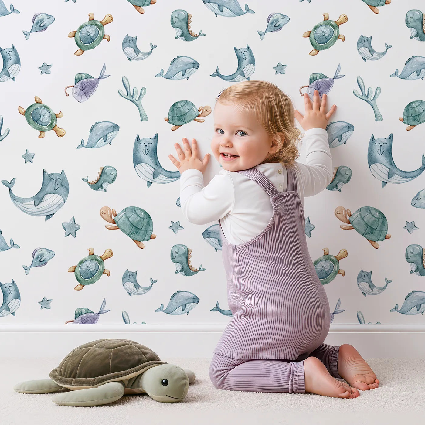 Lovely child standing in front of Whimsy Tots Dreamy Sea Pals Wallpaper in White with whale, turtle, fish, star, coral in design.