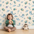 Lovely child standing in front of Whimsy Tots Dreamy Sea Pals Wallpaper in Beige with whale, turtle, fish, star, coral in design. Lovely child standing in front of Whimsy Tots Dreamy Sea Pals Wallpaper in Beige with whale, turtle, fish, star, coral in design.