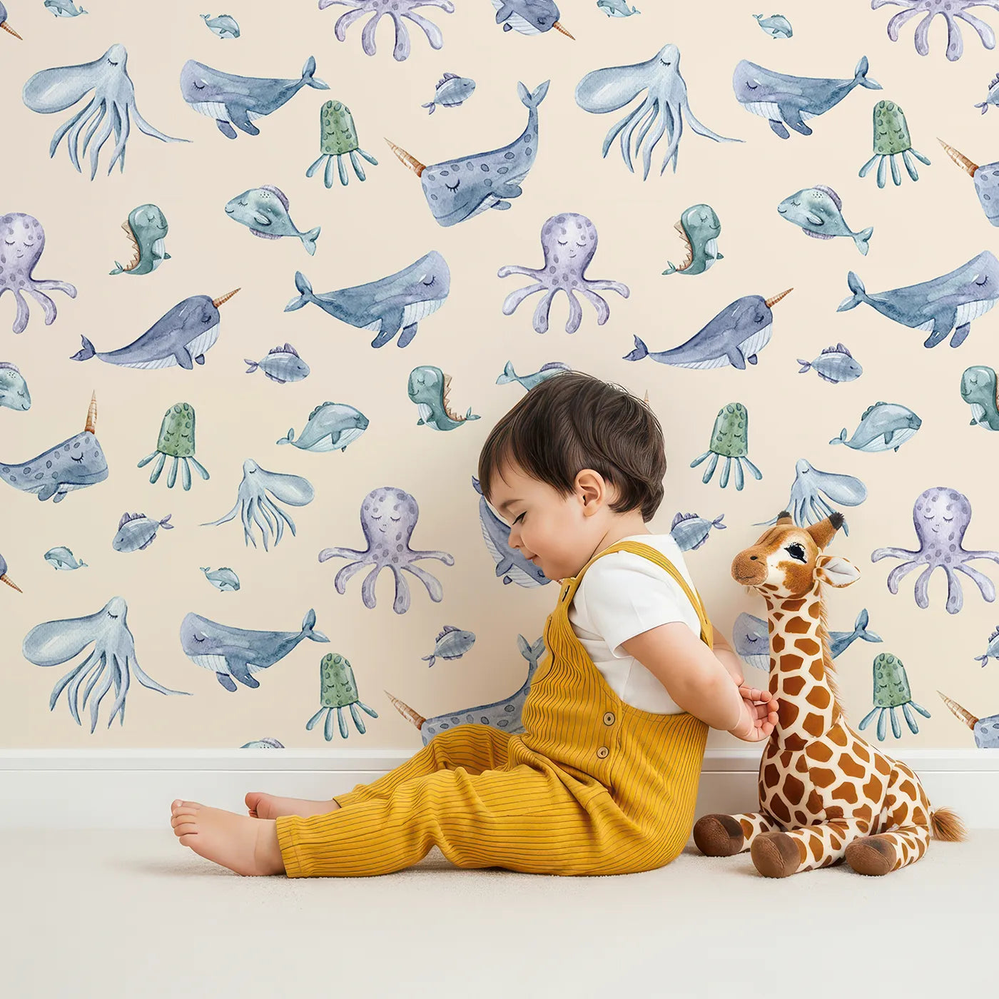 Lovely child standing in front of Whimsy Tots Whale Song Friends Wallpaper in Beige with whale, fish, narwhal, octopus, jellyfish in design.