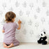 Lovely child standing in front of Whimsy Tots Petal Outline Grace Wallpaper in White with flower, leaf, sprig, botanical in design. Lovely child standing in front of Whimsy Tots Petal Outline Grace Wallpaper in White with flower, leaf, sprig, botanical in design.