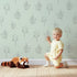 Lovely child standing in front of Whimsy Tots Petal Outline Grace Wallpaper in Mint Green with flower, leaf, sprig, botanical in design. Lovely child standing in front of Whimsy Tots Petal Outline Grace Wallpaper in Mint Green with flower, leaf, sprig, botanical in design.