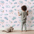 Lovely child standing in front of Whimsy Tots Cloudy Dreams Parade Wallpaper in Blush Pink with cloud, star, sheep, sky in design. Lovely child standing in front of Whimsy Tots Cloudy Dreams Parade Wallpaper in Blush Pink with cloud, star, sheep, sky in design.