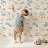 Lovely child standing in front of Whimsy Tots Cloudy Dreams Parade Wallpaper in Sand with cloud, star, sheep, sky in design. Lovely child standing in front of Whimsy Tots Cloudy Dreams Parade Wallpaper in Sand with cloud, star, sheep, sky in design.