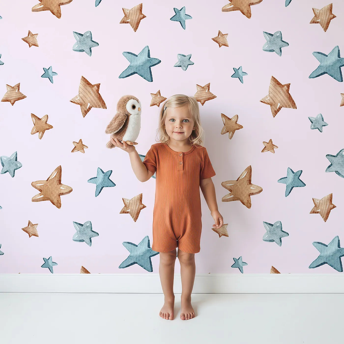 Lovely child standing in front of Whimsy Tots Starlight Scribbles Wallpaper in Blush Pink with star, scribble, doodle in design.