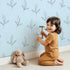 Lovely child standing in front of Whimsy Tots Whispering Leaflines Wallpaper in Blue with leaf, sprig, botanical, line art in design. Lovely child standing in front of Whimsy Tots Whispering Leaflines Wallpaper in Blue with leaf, sprig, botanical, line art in design.