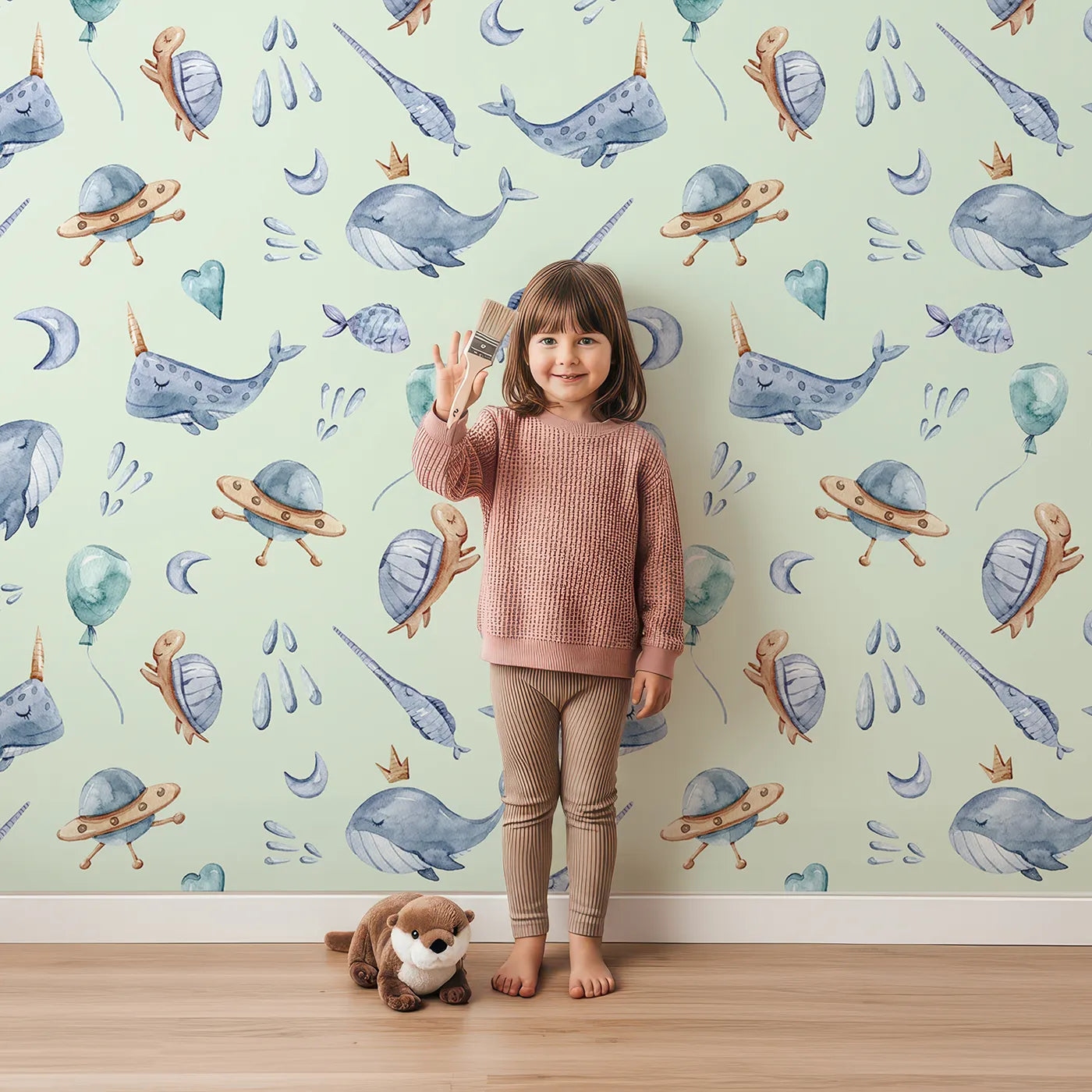 Lovely child standing in front of Whimsy Tots Galactic Ocean Friends Wallpaper in Mint Green with whale, turtle, narwhal, balloon, moon, UFO, droplet, crown in design.