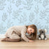 Lovely child standing in front of Whimsy Tots Wild Leafline Garden Wallpaper in Blue with leaf, botanical, sprig, berry, line art in design. Lovely child standing in front of Whimsy Tots Wild Leafline Garden Wallpaper in Blue with leaf, botanical, sprig, berry, line art in design.
