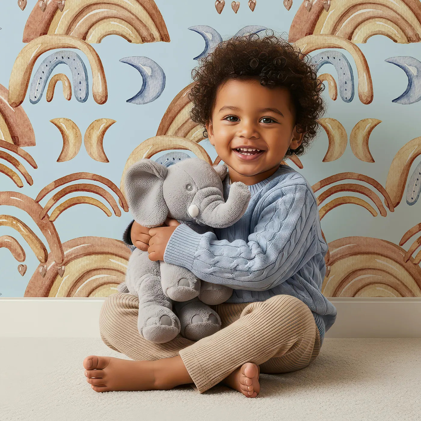 Lovely child standing in front of Whimsy Tots Boho Rainbow Night Wallpaper in Blue with rainbow, moon, heart, arch in design.