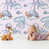 Lovely child standing in front of Whimsy Tots Ocean Cloud Cuddle Wallpaper in Blush Pink with turtle, octopus, fish, cloud, squid in design. Lovely child standing in front of Whimsy Tots Ocean Cloud Cuddle Wallpaper in Blush Pink with turtle, octopus, fish, cloud, squid in design.