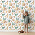 Lovely child standing in front of Whimsy Tots Lunar Lullaby Birds Wallpaper in White with bird, moon, heart in design. Lovely child standing in front of Whimsy Tots Lunar Lullaby Birds Wallpaper in White with bird, moon, heart in design.