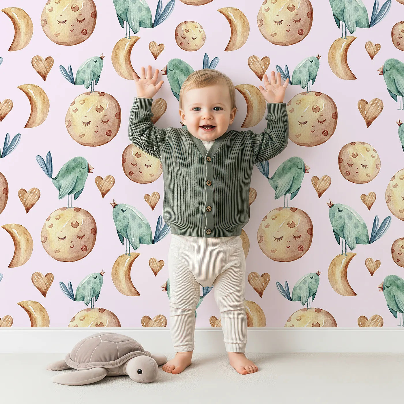 Lovely child standing in front of Whimsy Tots Lunar Lullaby Birds Wallpaper in Blush Pink with bird, moon, heart in design.