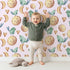 Lovely child standing in front of Whimsy Tots Lunar Lullaby Birds Wallpaper in Blush Pink with bird, moon, heart in design. Lovely child standing in front of Whimsy Tots Lunar Lullaby Birds Wallpaper in Blush Pink with bird, moon, heart in design.