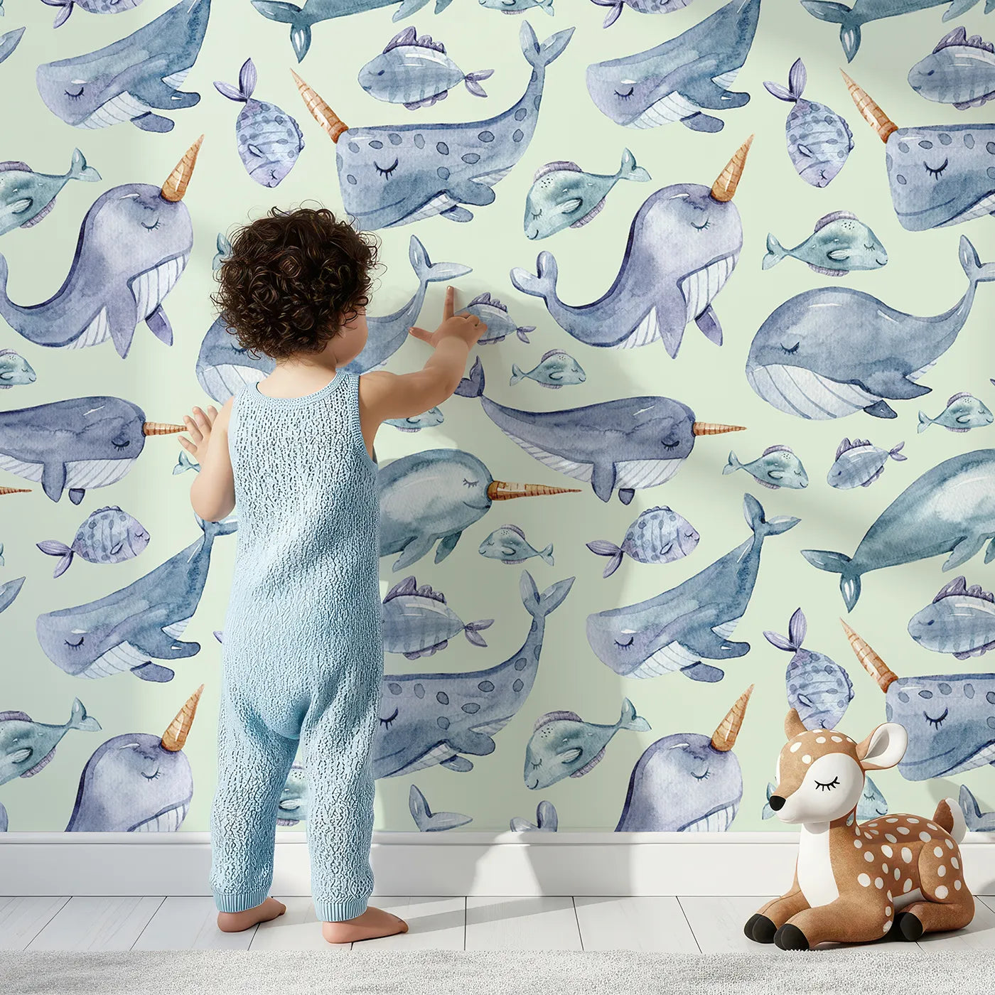 Lovely child standing in front of Whimsy Tots Sleepy Sea Friends Wallpaper in Mint Green with whale, narwhal, fish in design.