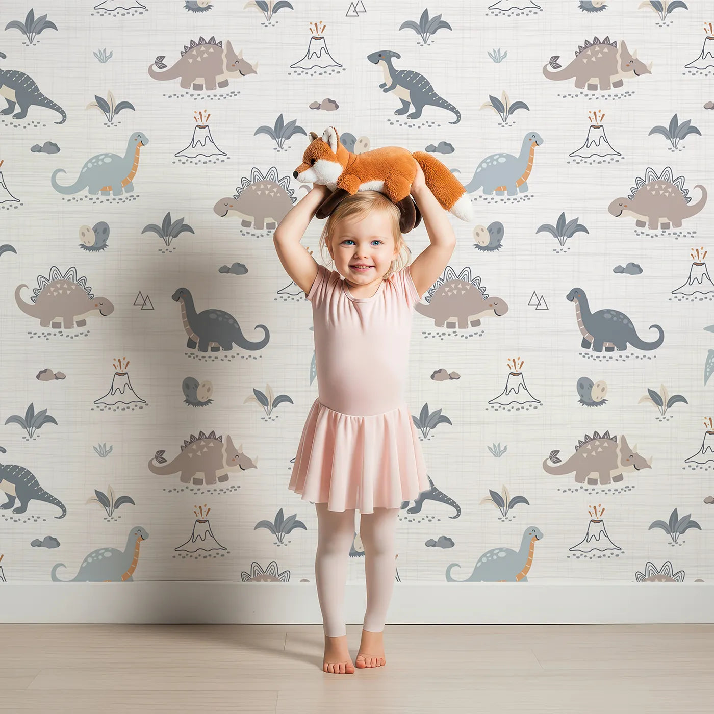 Lovely child standing in front of Whimsy Tots Prehistoric Pals Volcano Wallpaper with dinosaur, volcano, egg, rock, plant in design.