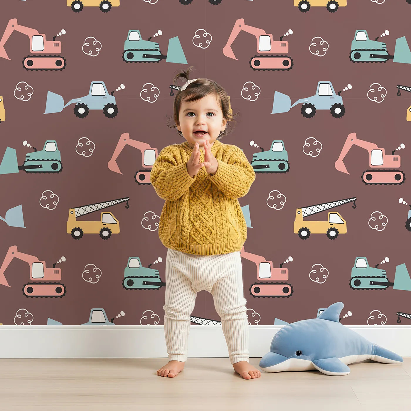 Lovely child standing in front of Whimsy Tots Mighty Machines Construction Wallpaper with truck, crane, excavator, bulldozer, vehicle in design.