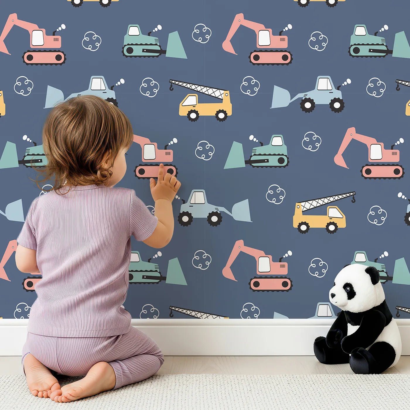 Lovely child standing in front of Whimsy Tots Mighty Machines Construction Wallpaper in Navy Blue with truck, crane, bulldozer, excavator, vehicle in design.
