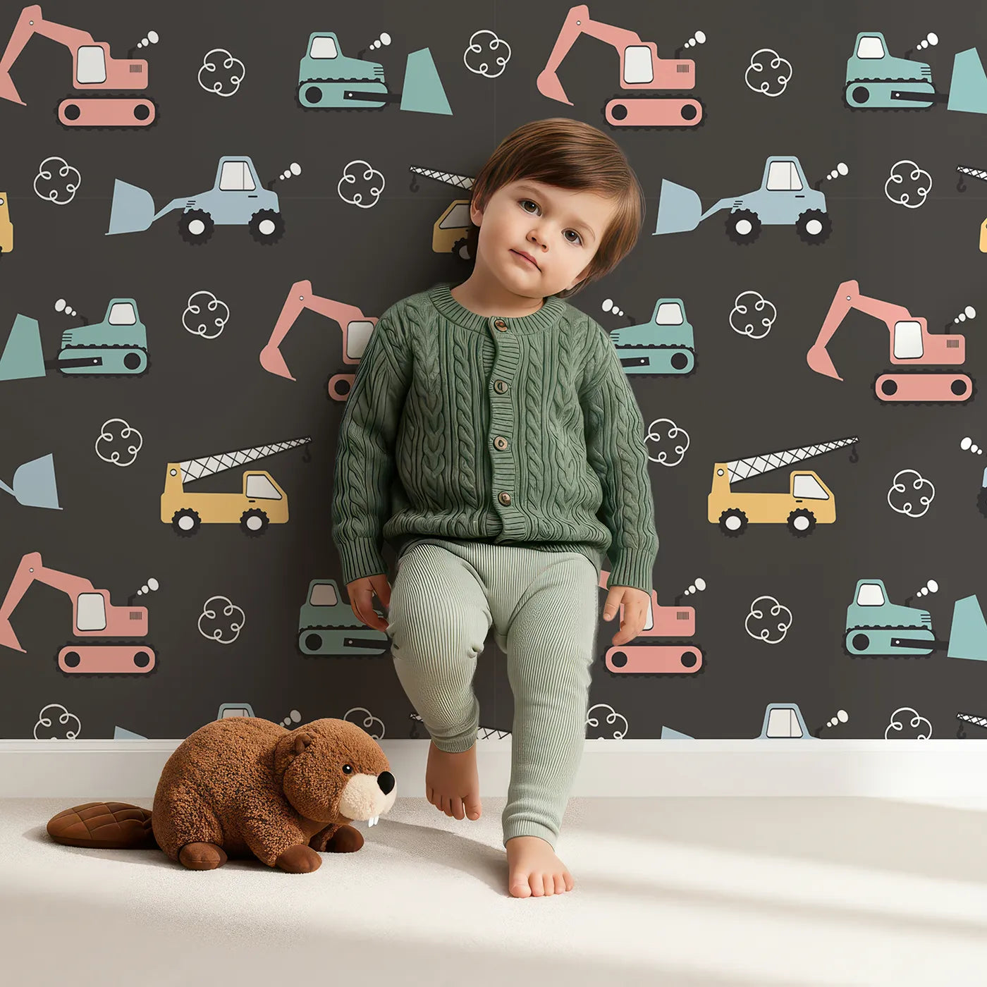 Lovely child standing in front of Whimsy Tots Mighty Machines Construction Wallpaper in Charcoal Gray with truck, crane, bulldozer, excavator, vehicle in design.