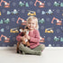 Lovely child standing in front of Whimsy Tots Mighty Machines Construction Wallpaper in Denim with truck, crane, bulldozer, excavator, vehicle in design. Lovely child standing in front of Whimsy Tots Mighty Machines Construction Wallpaper in Denim with truck, crane, bulldozer, excavator, vehicle in design.