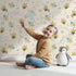 Lovely child standing in front of Whimsy Tots Busy Bees at Play Wallpaper in Sand with bee, heart, honey, flower, leaf in design. Lovely child standing in front of Whimsy Tots Busy Bees at Play Wallpaper in Sand with bee, heart, honey, flower, leaf in design.
