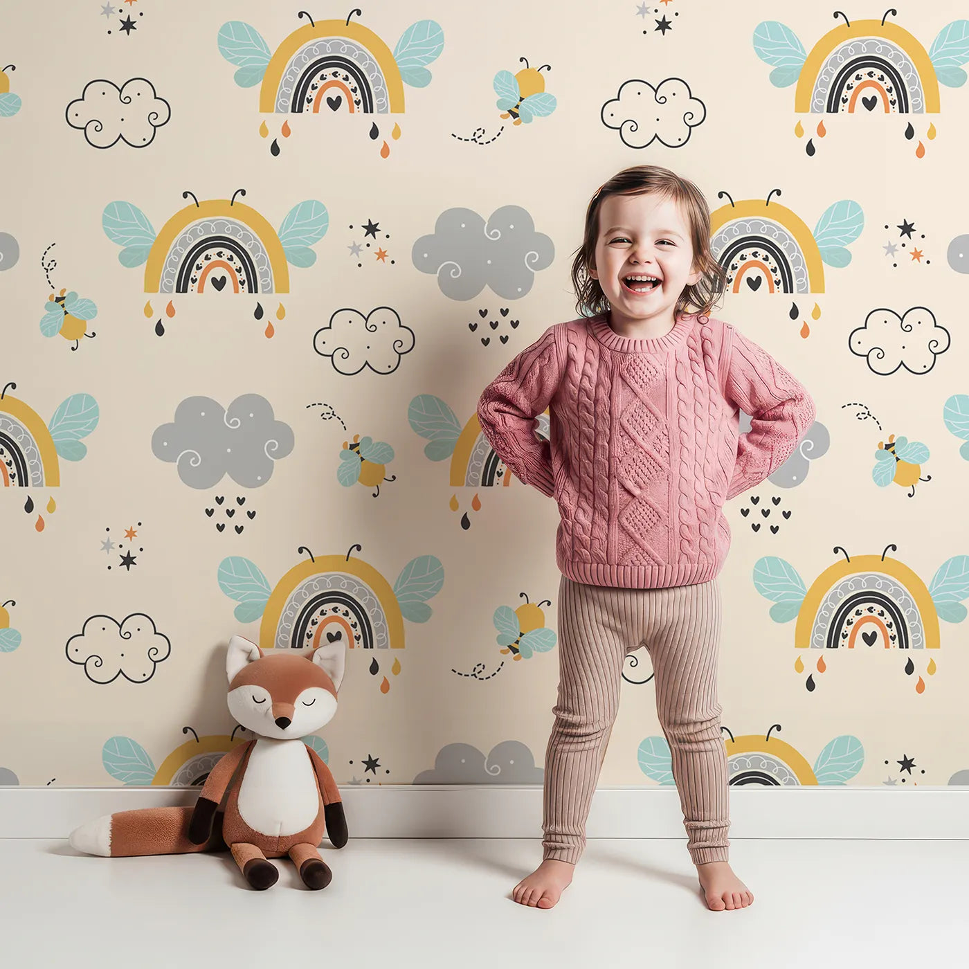 Lovely child standing in front of Whimsy Tots Bee Rainbow Dreams Wallpaper in Sand with bee, rainbow, star, cloud in design.