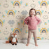 Lovely child standing in front of Whimsy Tots Bee Rainbow Dreams Wallpaper in Sand with bee, rainbow, star, cloud in design. Lovely child standing in front of Whimsy Tots Bee Rainbow Dreams Wallpaper in Sand with bee, rainbow, star, cloud in design.