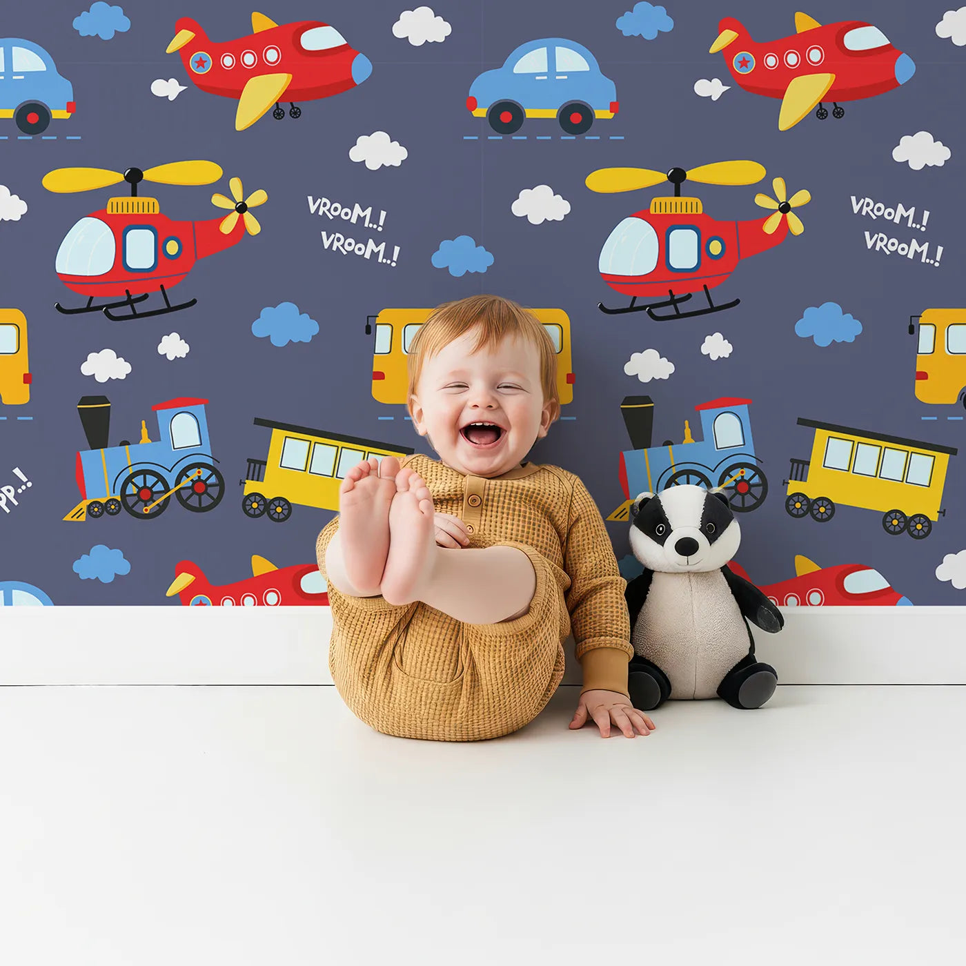 Lovely child standing in front of Whimsy Tots Vroom Vroom Transport Parade Wallpaper in Denim with bus, train, plane, car, helicopter, cloud in design.