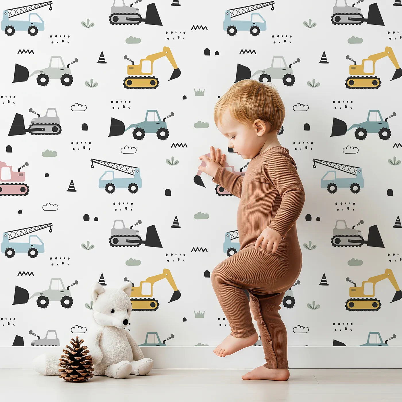 Lovely child standing in front of Whimsy Tots Digger Parade Wallpaper in White with crane, digger, loader, truck, cone in design.