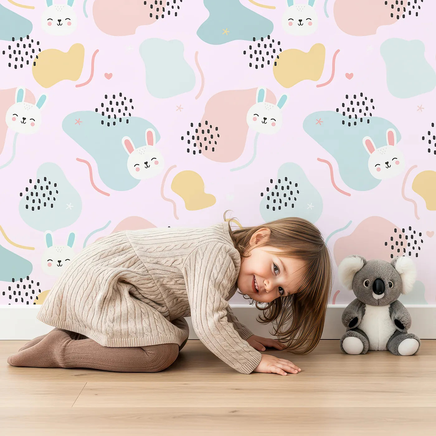 Lovely child standing in front of Whimsy Tots Bunny Bounce Abstract Wallpaper in Blush Pink with bunny, blob, heart, texture in design.