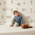 Lovely child standing in front of Whimsy Tots Sleepy Safari Snuggles Wallpaper in Cream with elephant, zebra, lion, giraffe, hippo, tree, flower in design. Lovely child standing in front of Whimsy Tots Sleepy Safari Snuggles Wallpaper in Cream with elephant, zebra, lion, giraffe, hippo, tree, flower in design.