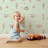 Lovely child standing in front of Whimsy Tots Sleepy Safari Snuggles Wallpaper in Mint Green with elephant, zebra, lion, giraffe, hippo, tree, flower in design. Lovely child standing in front of Whimsy Tots Sleepy Safari Snuggles Wallpaper in Mint Green with elephant, zebra, lion, giraffe, hippo, tree, flower in design.