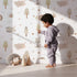 Lovely child standing in front of Whimsy Tots Sleepy Safari Snuggles Wallpaper in Soft White with elephant, zebra, lion, giraffe, hippo, tree, flower in design. Lovely child standing in front of Whimsy Tots Sleepy Safari Snuggles Wallpaper in Soft White with elephant, zebra, lion, giraffe, hippo, tree, flower in design.