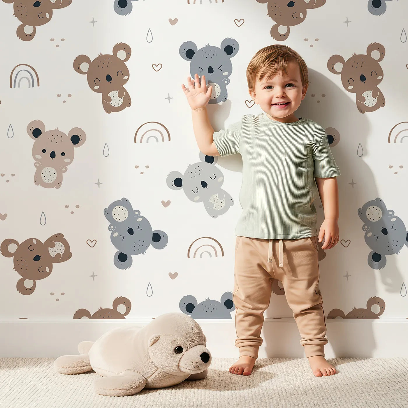 Lovely child standing in front of Whimsy Tots Koala Cuddle Parade Wallpaper in White with koala, rainbow, heart, raindrop in design.