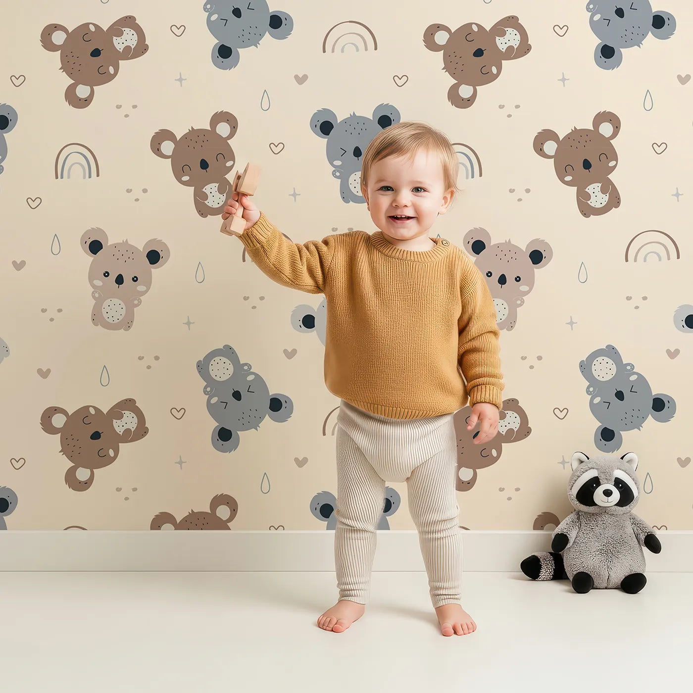 Lovely child standing in front of Whimsy Tots Koala Cuddle Parade Wallpaper in Beige with koala, rainbow, heart, raindrop in design.