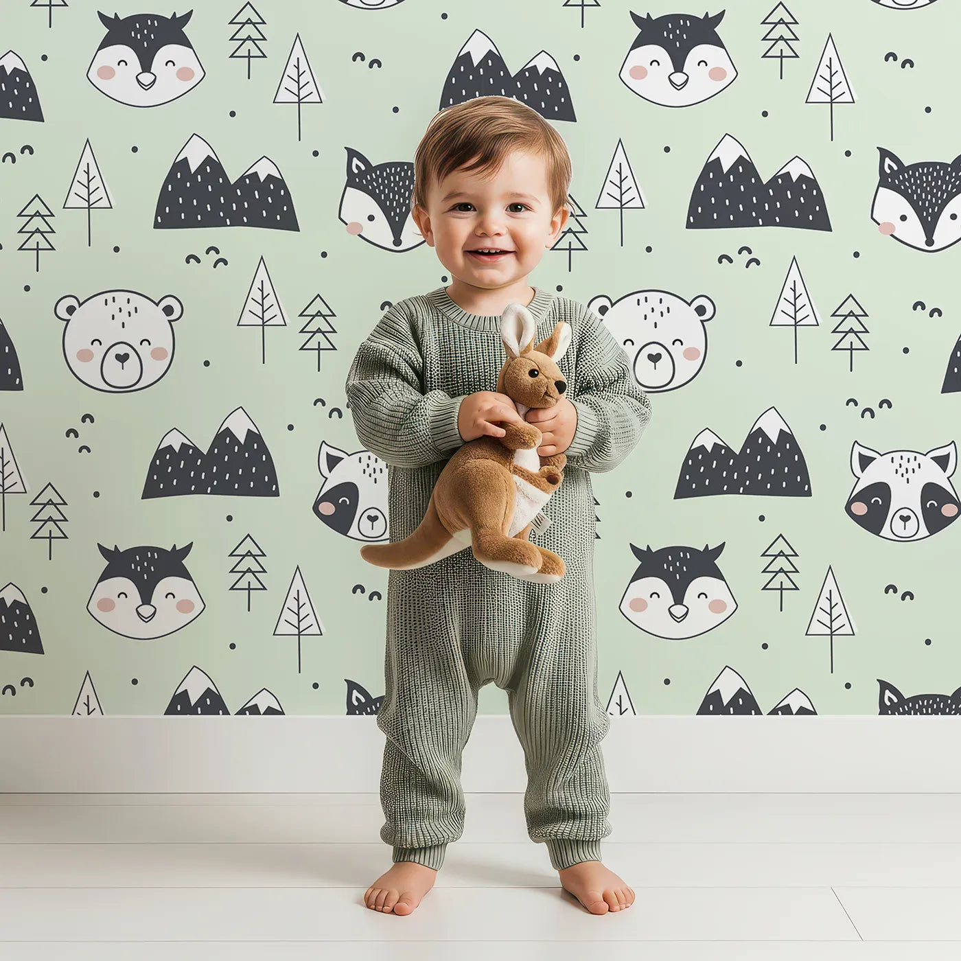 Lovely child standing in front of Whimsy Tots Woodland Peekaboo Friends Wallpaper in Mint Green with bear, owl, fox, raccoon, mountain, tree in design.