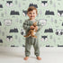 Lovely child standing in front of Whimsy Tots Woodland Peekaboo Friends Wallpaper in Mint Green with bear, owl, fox, raccoon, mountain, tree in design. Lovely child standing in front of Whimsy Tots Woodland Peekaboo Friends Wallpaper in Mint Green with bear, owl, fox, raccoon, mountain, tree in design.