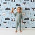 Lovely child standing in front of Whimsy Tots Woodland Peekaboo Friends Wallpaper in Blue with bear, owl, fox, raccoon, mountain, tree in design. Lovely child standing in front of Whimsy Tots Woodland Peekaboo Friends Wallpaper in Blue with bear, owl, fox, raccoon, mountain, tree in design.