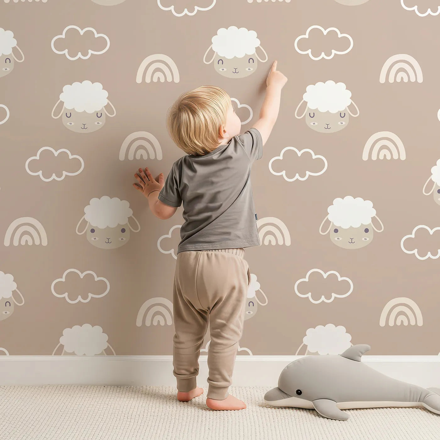 Lovely child standing in front of Whimsy Tots Sleepy Lamb Skies Wallpaper in Taupe Beige with sheep, cloud, rainbow in design.