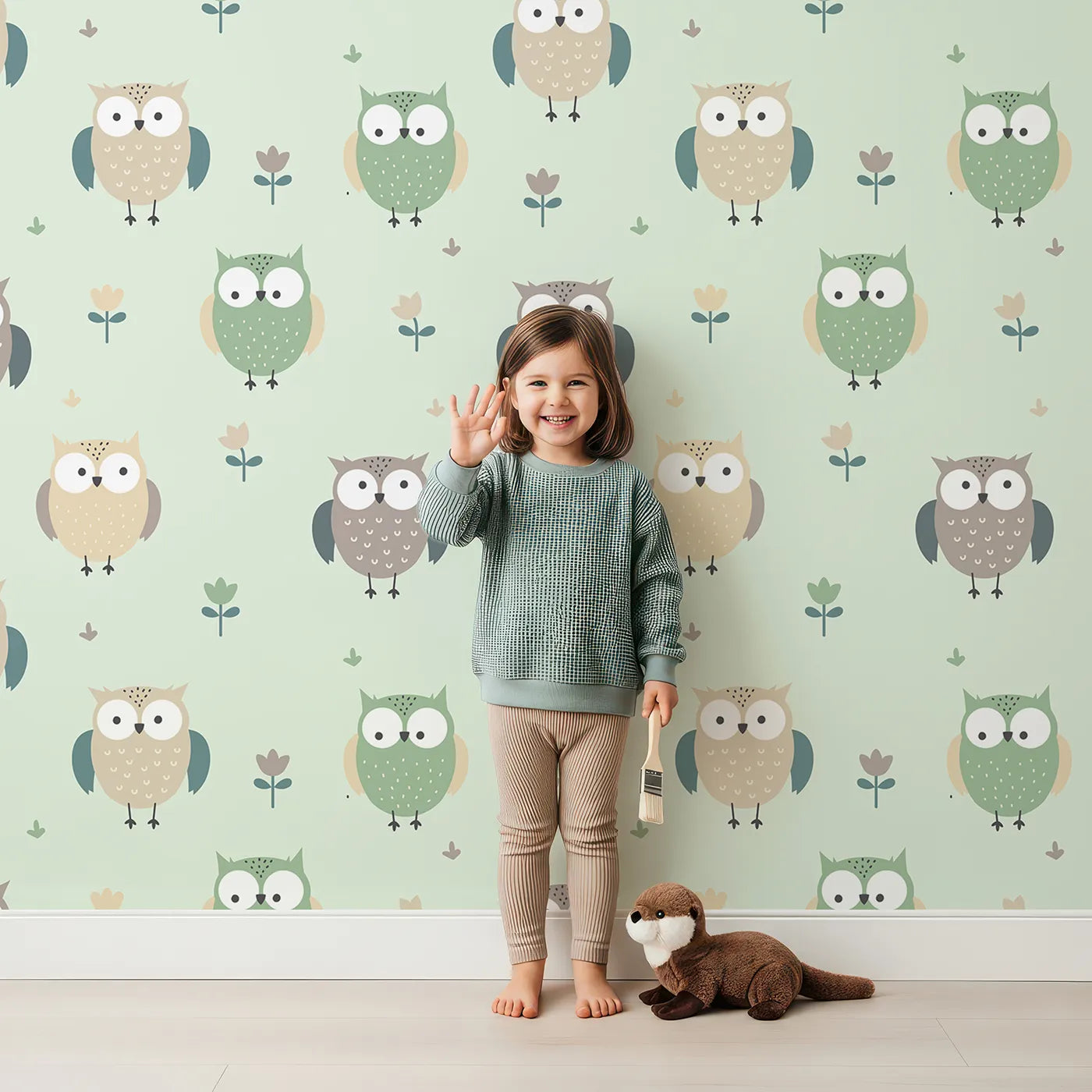 Lovely child standing in front of Whimsy Tots Gentle Owl Garden Wallpaper in Misty Green with owl, flower, leaf in design.