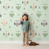 Lovely child standing in front of Whimsy Tots Gentle Owl Garden Wallpaper in Misty Green with owl, flower, leaf in design. Lovely child standing in front of Whimsy Tots Gentle Owl Garden Wallpaper in Misty Green with owl, flower, leaf in design.